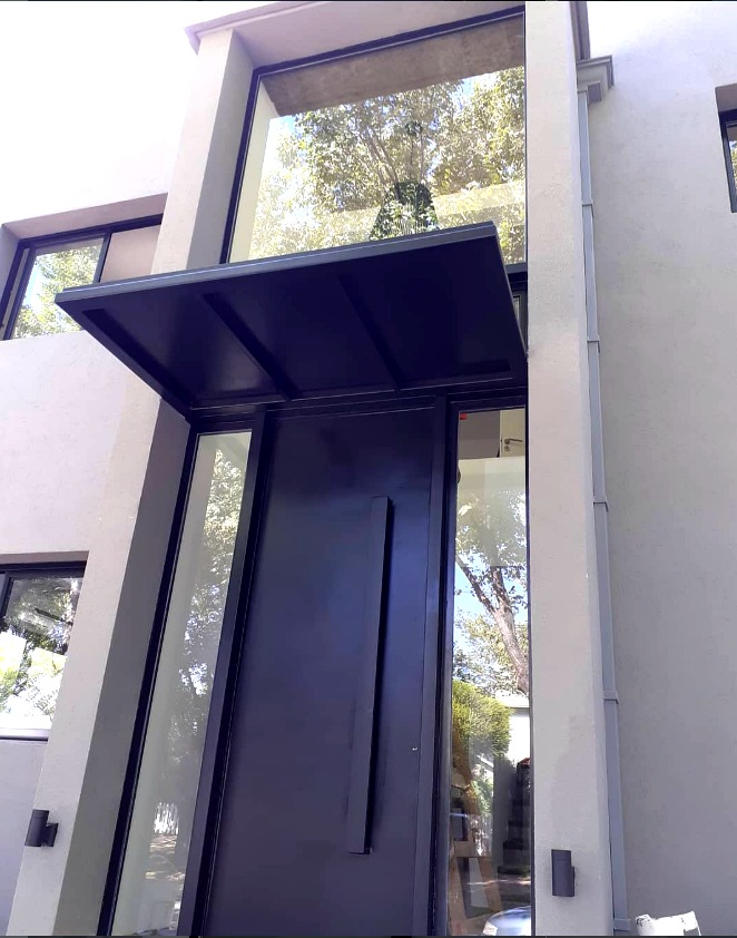 Puerta principal negra con marquesina y paños de vidrio